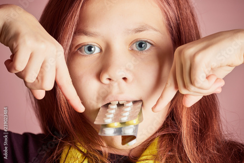 Beautiful girl with blue eyes holds in her teeth pack of pills from disease and points fingers at them.