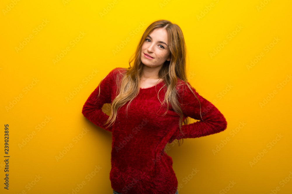 Fototapeta premium Young girl on vibrant yellow background suffering from backache for having made an effort