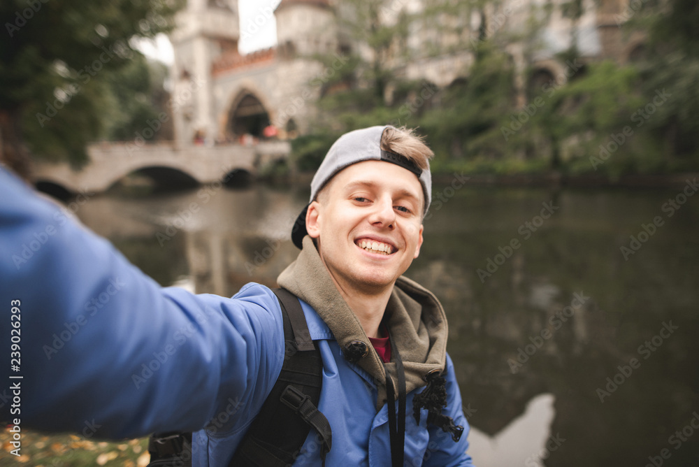 Φωτογραφία Young lucky tourist makes a sephi on the background of the lake and the castle and smiles