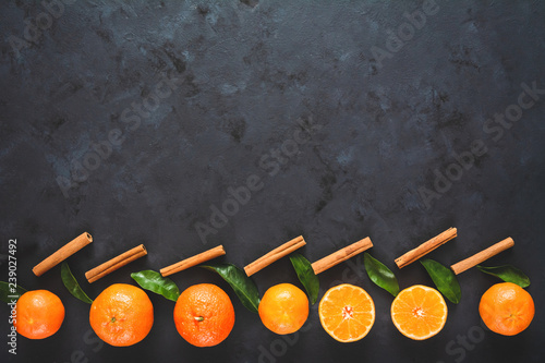 Tangerines (oranges, clementines) with green leaves on black background. Copy space, top view.