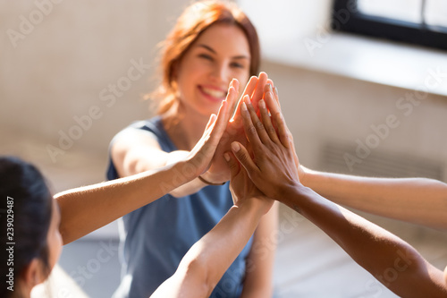 Quadro su tela Cheerful diverse young girls sitting together in sports studio before starts training giving high five feel happy and healthy, close up focus on hands