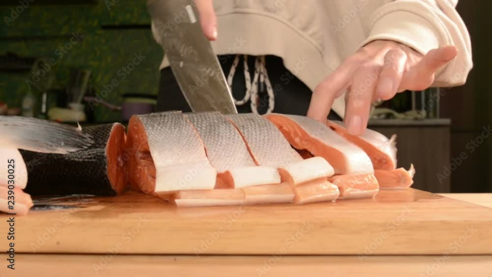 Close-up of female hands are cutting with a knife a large salmon on a wooden table of home cooking Close-up of female hands are cutting with a knife a large salmon on a wooden table of home cooking