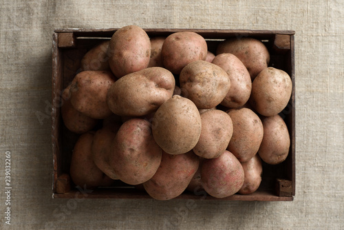 a pile of fresh potatoes in a dark wooden box. Linen canvas background.