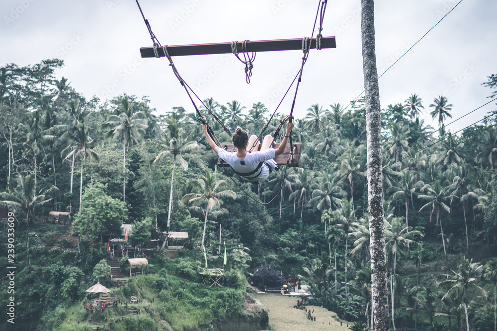 Young woman tourist swinging in the jungle of Bali island.