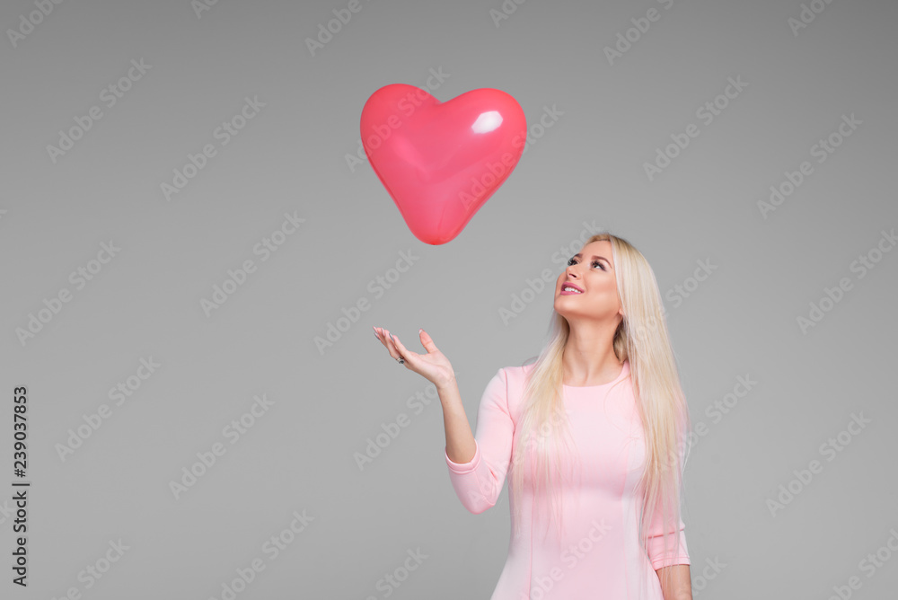 Beautiful young blond woman with pink heart shape air balloon on grey background. Woman on Valentine's Day. Symbol of love - Image. Space for text Beautiful young blond woman with pink heart shape air balloon on grey background. Woman on Valentine's Day. Symbol of love - Image. Space for text