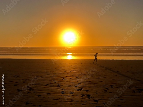 Running silhouette at sunset along golden beach