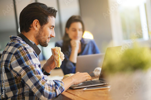 Foto Attractive man eating sandwich whilst working in co working space