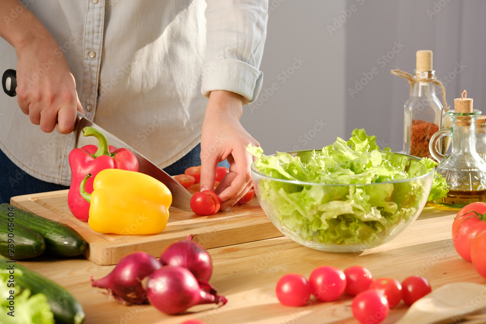 Girl cuts fresh tomatoes for a delicious salad. A variety of fresh vegetables on a wooden table. Girl cuts fresh tomatoes for a delicious salad. A variety of fresh vegetables on a wooden table.