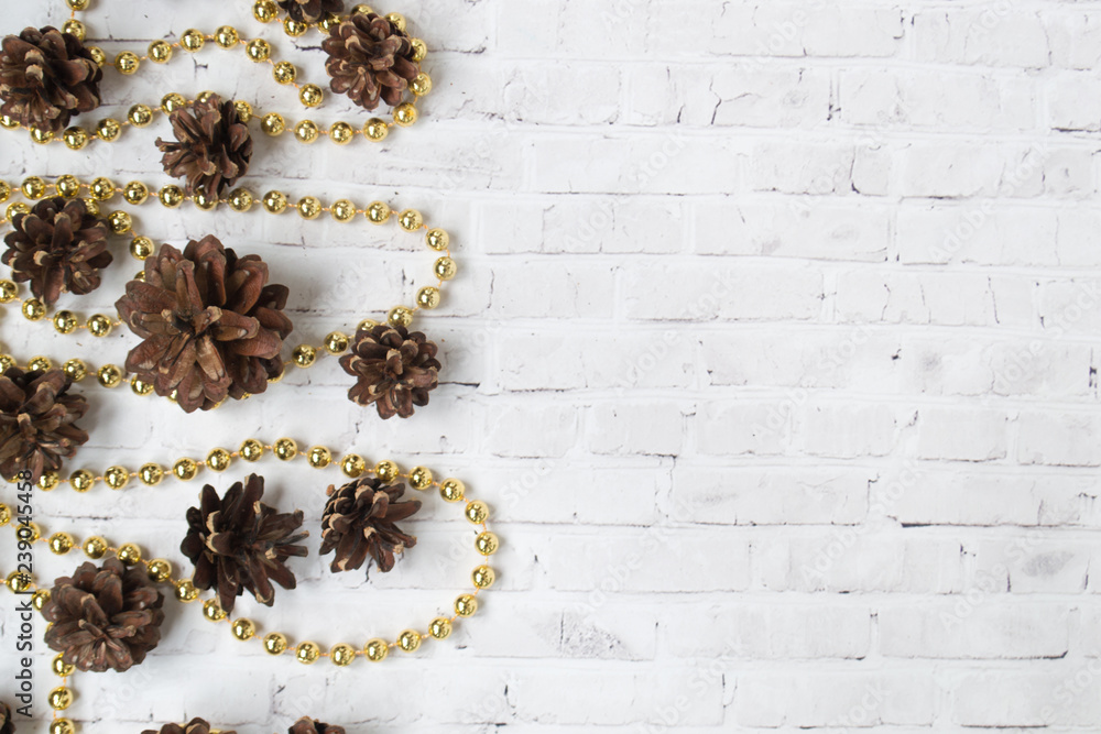 Light, white brick background with brown fir cones and golden garlands lying in the loose Light, white brick background with brown fir cones and golden garlands lying in the loose