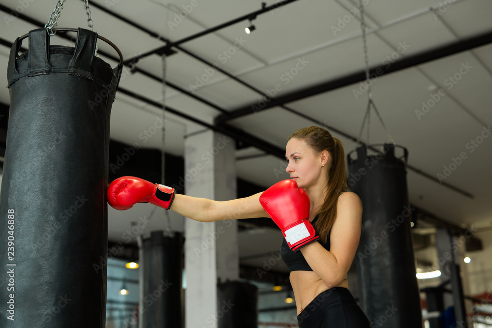 beautiful young girl is engaged in boxing with a punching bag in the gym