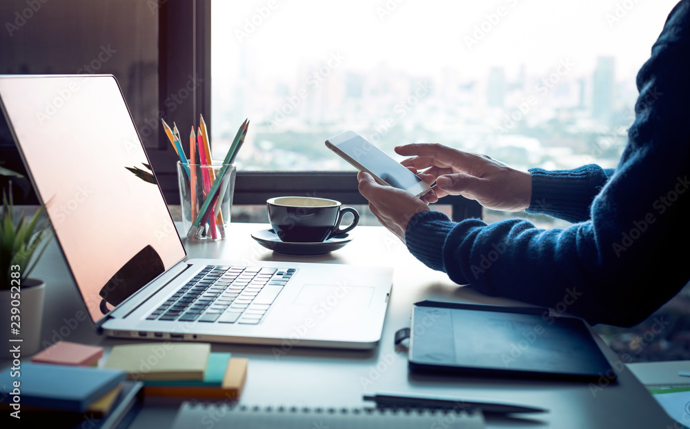 Fototapeta premium Young man using smartphone with modern work table and computer laptop and cityscapes view from window.Business concepts ideas.Strategy analysis