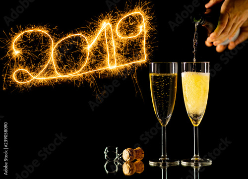 Glasses of champagne and New Year 2019 golden numbers written with Sparkle fireworks on black