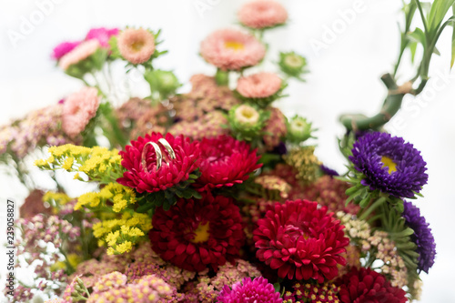 two gold rings of bride and groom on top of a flower of a colorful bouquet of flowers