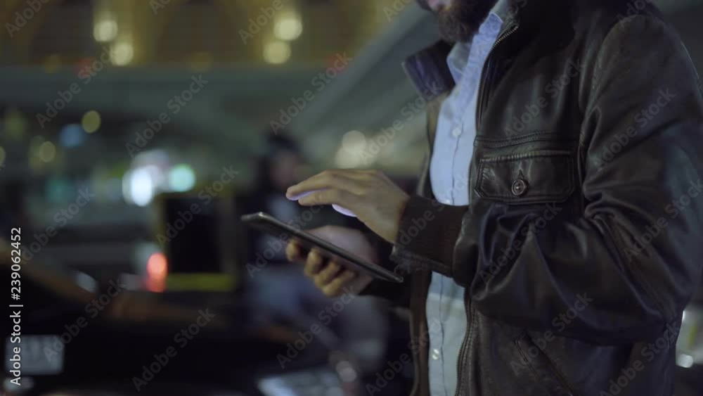 Young man texting on tablet while walking on street at night, cropped shot. Side view of freelancer using digital device in city with copy space. Communication concept Young man texting on tablet while walking on street at night, cropped shot. Side view of freelancer using digital device in city with copy space. Communication concept