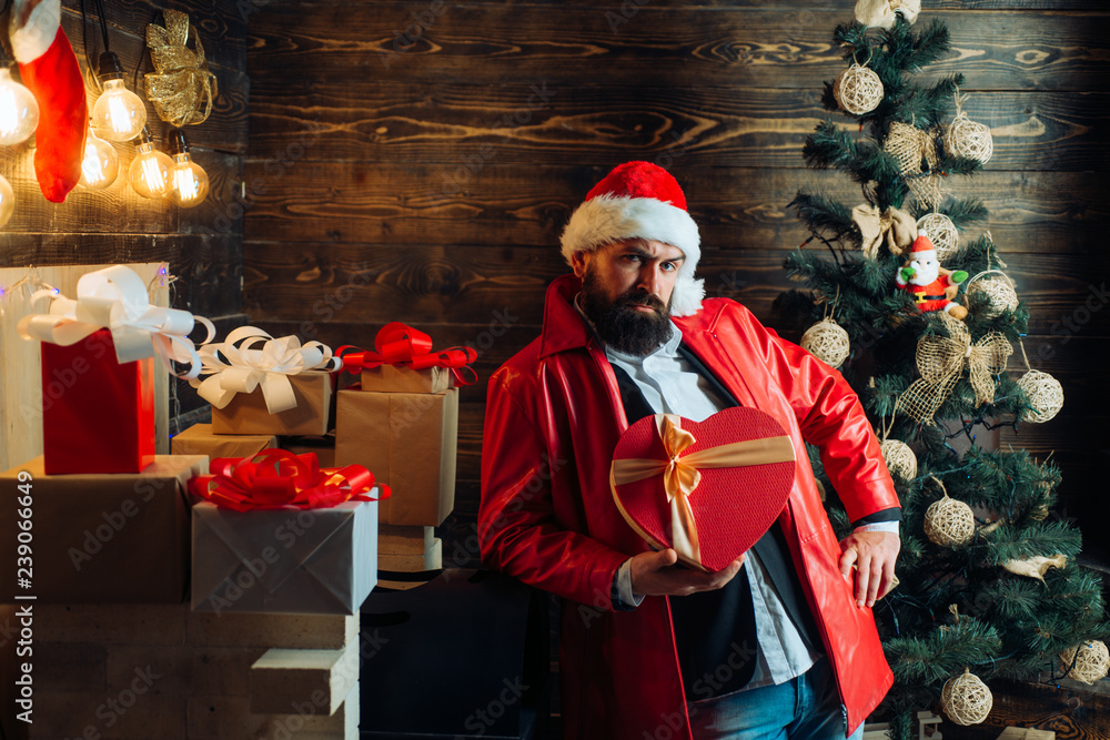 Bearded modern santa wishes Merry christmas and Happy new year. Christmas Celebration, holiday. Christmas tree background. Santa claus with red Christmas gift box.
