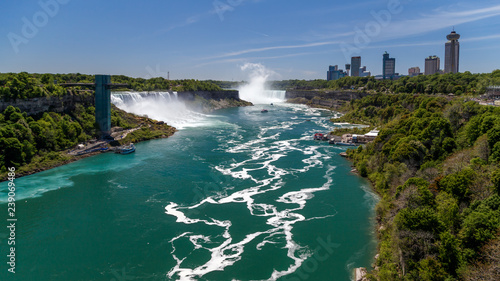 Niagara Falls, looking down the Niagara river. Panoramic view of the river, observation tower, the deck with tourist, watefalls, cruise boats, city skyline. Travel USA.