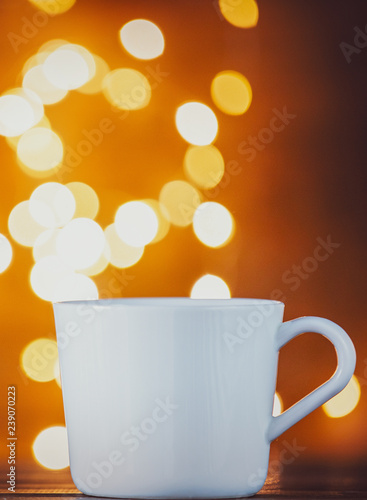 White cup of tea or coffee and Christmas Lights on background