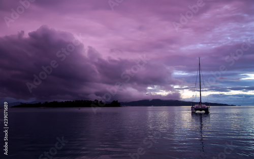 Lonely catamaran at sunset against the background of storm clouds near small islands in the Pacific ocean, French Polynesia.