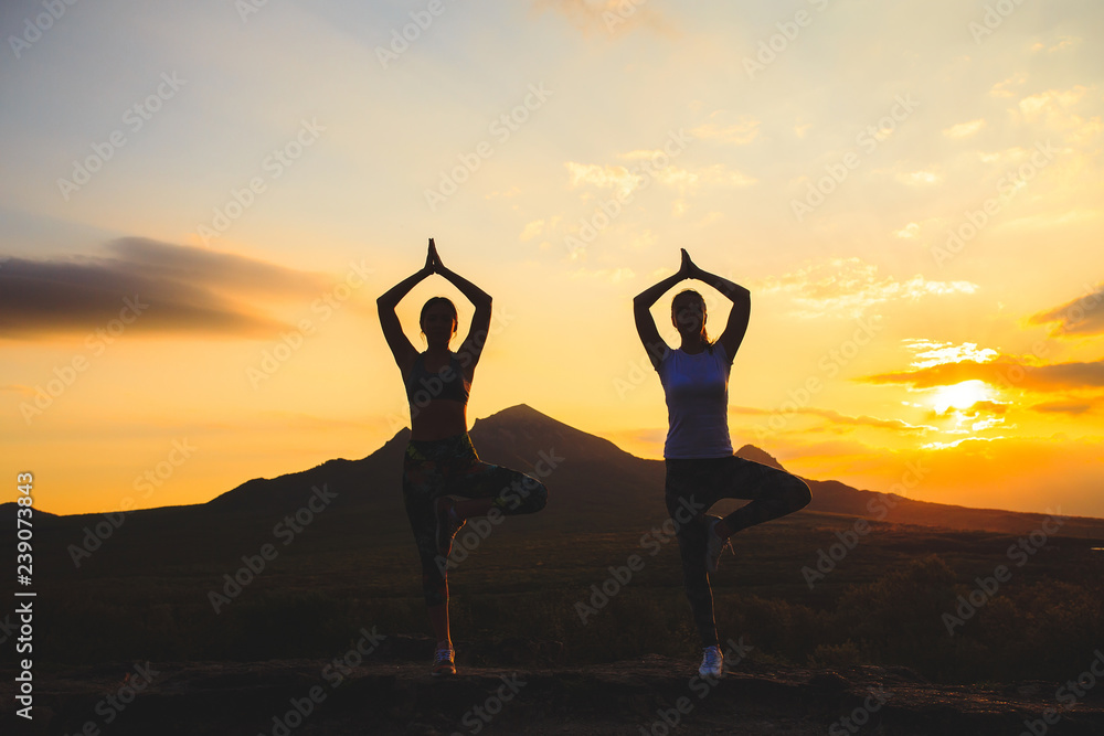 Silhouette of young womans practicing yoga or pilates at sunset or sunrise in beautiful mountain location. Silhouette of young womans practicing yoga or pilates at sunset or sunrise in beautiful mountain location.