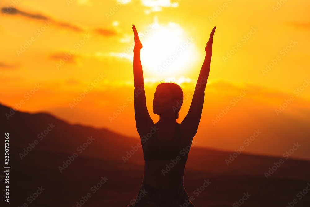 Silhouette of young woman practicing yoga or pilates at sunset or sunrise in beautiful mountain location. Silhouette of young woman practicing yoga or pilates at sunset or sunrise in beautiful mountain location.