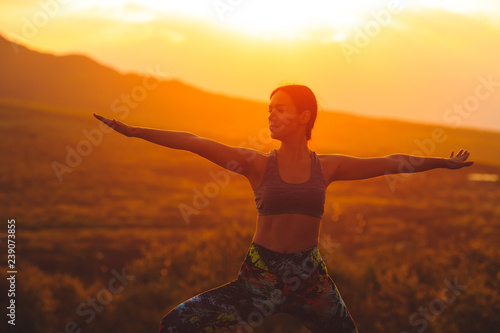 Silhouette of young woman practicing yoga or pilates at sunset or sunrise in beautiful mountain location. © davit85