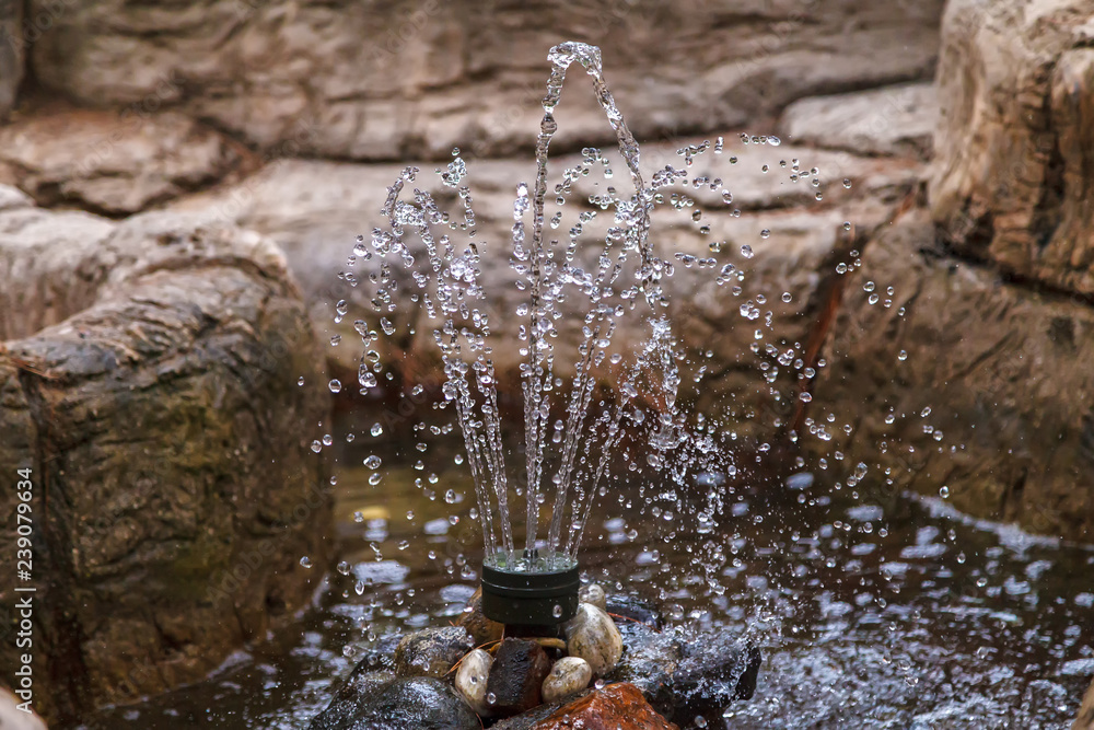 A small decorative fountain among the stones in the city park. Short shutter speed