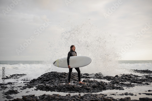 Photography Brunette guy standing with a surf in his hands on the shore on the day