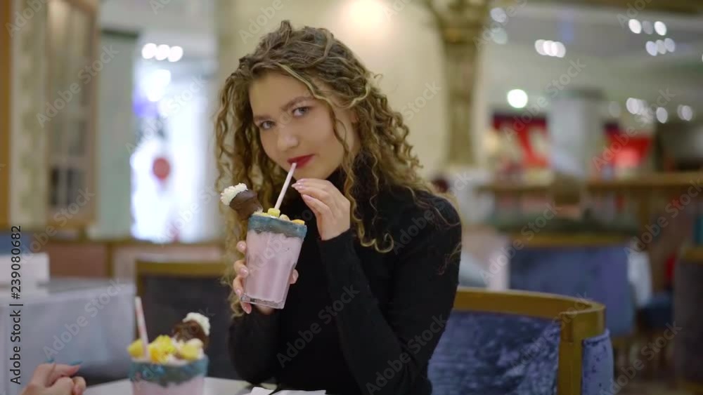 pretty young woman is sipping tasty milkshake with whipped cream and ice cream sitting in cafe pretty young woman is sipping tasty milkshake with whipped cream and ice cream sitting in cafe