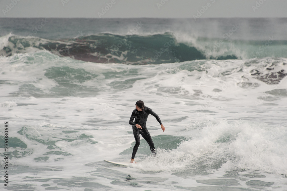 Brunette man in the black swimsuit riding on a surf on the sea