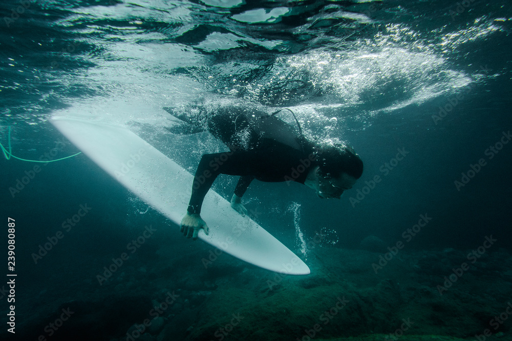 Obraz premium Guy holding a surf board dive under the wave