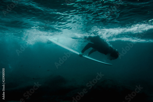 Boy in the black swimsuit flowing down holding a surf board dive under the wave