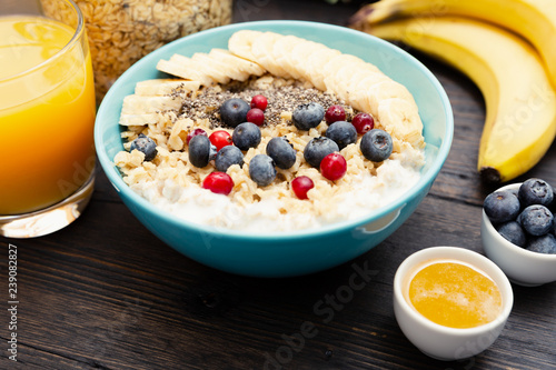 Healthy fitness breakfast: oatmeal with bananas, blueberries and cranberries, chia seeds and yogurt on dark wooden board with texture