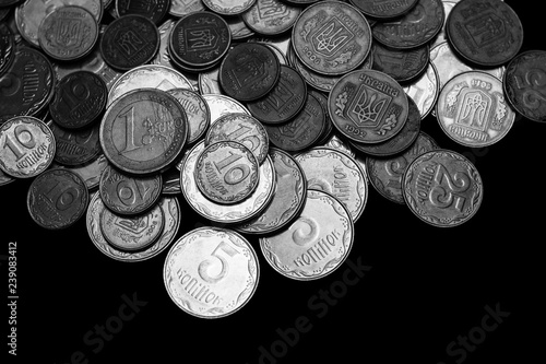 Ukrainian coins with one euro coin isolated on black background. Black and white image. Close-up view. Coins are located at the upper side of frame. A conceptual image.