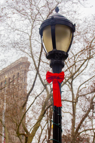 Lamppost with red bow decorated for Christmas with Flatiron Building in background seen from Madison Square Park, New York City Manhattan