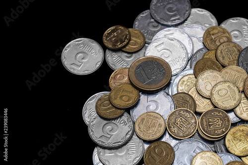 Ukrainian coins with one euro coin isolated on black background. Close-up view. Coins are located at the right side of frame. A conceptual image.