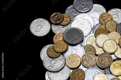Ukrainian coins with one euro coin isolated on black background. Euro coin is uncolored. Close-up view. Coins are located at the right side of frame. A conceptual image.