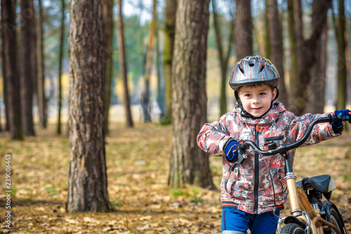 Happy kid boy of 3 or 5 years having fun in autumn forest with a bicycle on beautiful fall day. Active child wearing bike helmet. Safety, sports, leisure with kids concept.