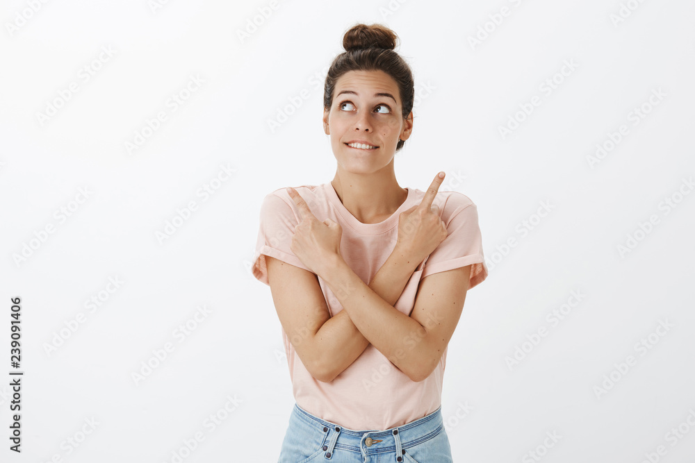 Obraz premium Girl wanting to buy new thing standing hesitant fighting desire to spend money on good product biting lower lip from want and interest pointing sideways as gazing at upper left corner dreamy