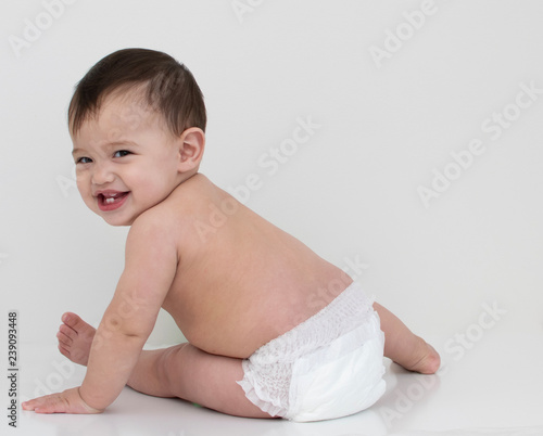 Baby wear white diaper sit aside and turn his face with smile  in white background 