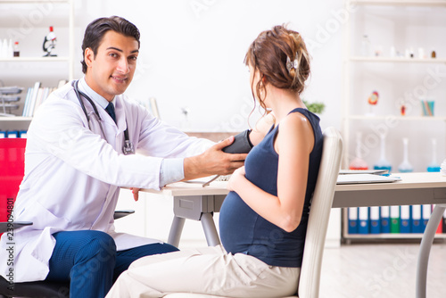 Young doctor checking pregnant woman s blood pressure