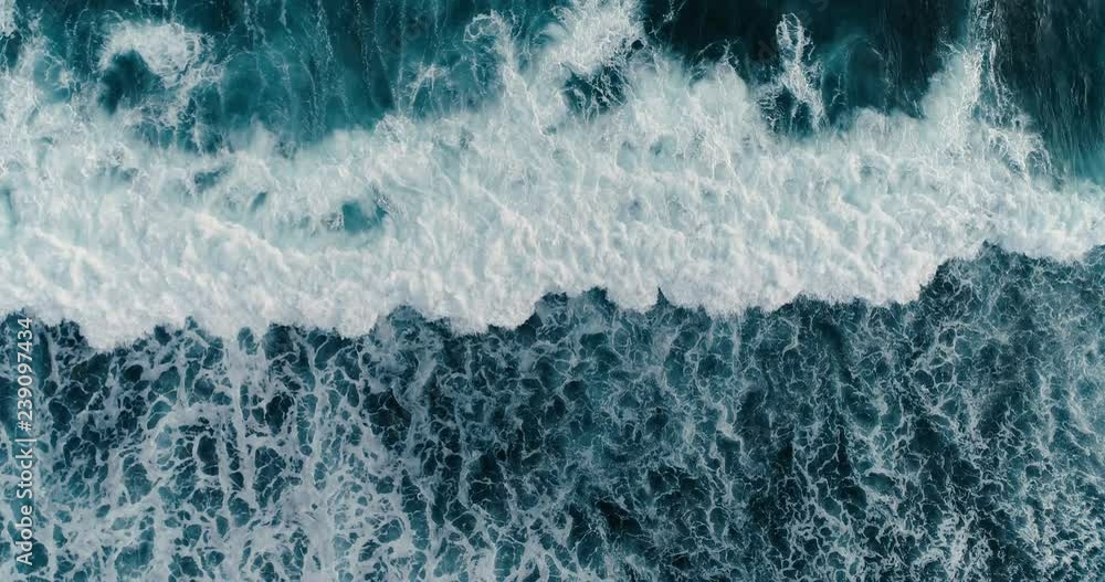 Aerial headover drone footage of huge waves crashing on dark sand of the coast 4K