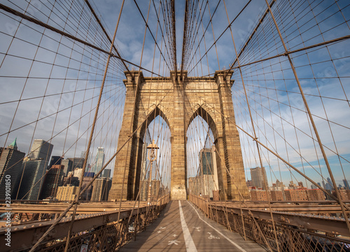 The Upper Deck Walkway of the Brooklyn Bridge Facing the Manhattan Skyline During a Clear Sunny Day © porqueno