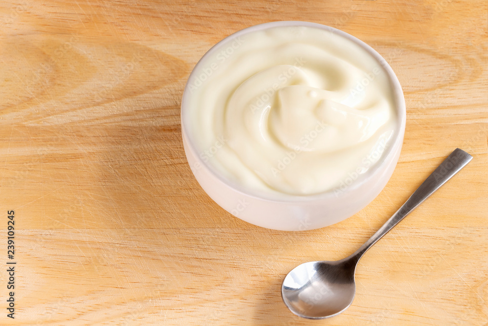 Bowl of yogurt and spoon on the wood table. Yogurt made from milk fermented by added bacteria, often sweetened and flavored. Bowl of yogurt and spoon on the wood table. Yogurt made from milk fermented by added bacteria, often sweetened and flavored.