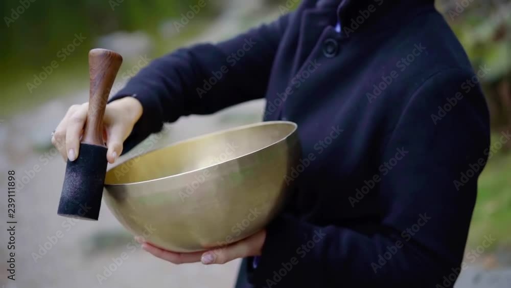 Close up shooting of a meditating woman playing on a bronze tibetan singins bowl outdoor in nature. Close up shooting of a meditating woman playing on a bronze tibetan singins bowl outdoor in nature.