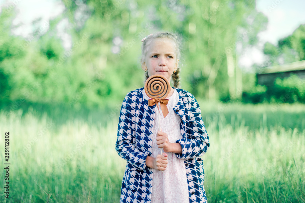 Fototapeta premium Little girl with pigtails and a big lollipop on a green summer background