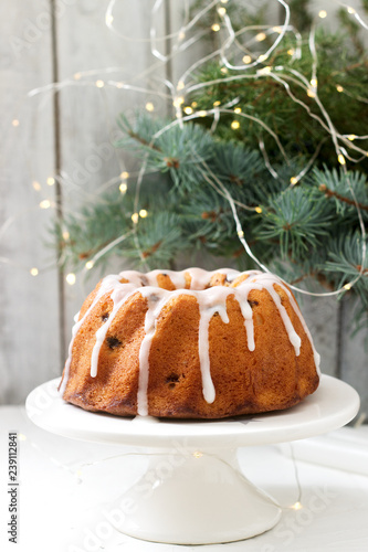 Pie with raisins and icing from powdered sugar on the background of fir branches and garlands. Rustic style. photo