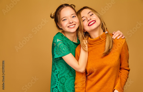 Two young beautiful blond smiling hipster girls posing in trendy summer clothes. Carefree women isolated on golden background. Positive models going crazy