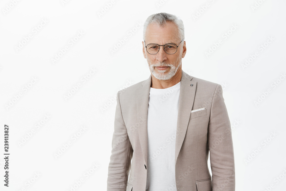 Self-assured smart and intelligent senior rich businessman in glasses an elegant suit standing confident and looking at camera focused and determined ready accomplish anything over grey wall Self-assured smart and intelligent senior rich businessman in glasses an elegant suit standing confident and looking at camera focused and determined ready accomplish anything over grey wall