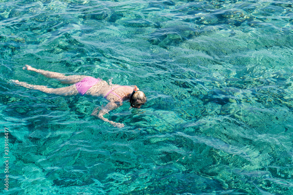 Young girl snorkeling in tropical water on vacation. Woman swimming in blue sea. Snorkeling girl in full-face snorkeling mask.