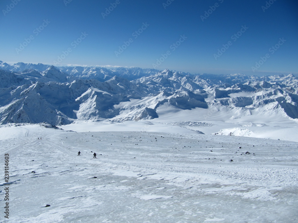 Beautiful views of the ridge and mountain peaks. Snowboarders go down the slope off the road.